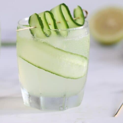 green gin cocktail in a cup with cucumber garnish