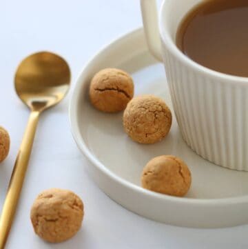 peanut butter cookie balls on a plate with a cup of coffee and a teaspoon