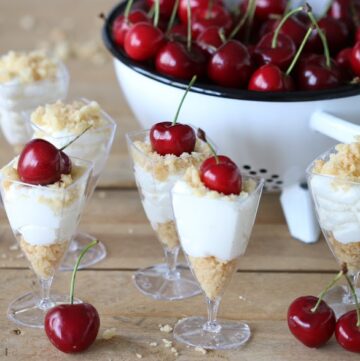 individual crumb cheese cake in a serving cups with cherries garnish