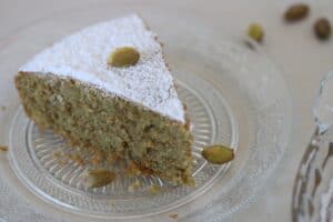 pistachio cake slice garnished with powdered sugar and shelled pistachios on a plate