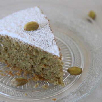 pistachio cake slice garnished with powdered sugar and shelled pistachios on a plate